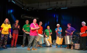 group of people playing drums in a samba class all standing up in a broken line.